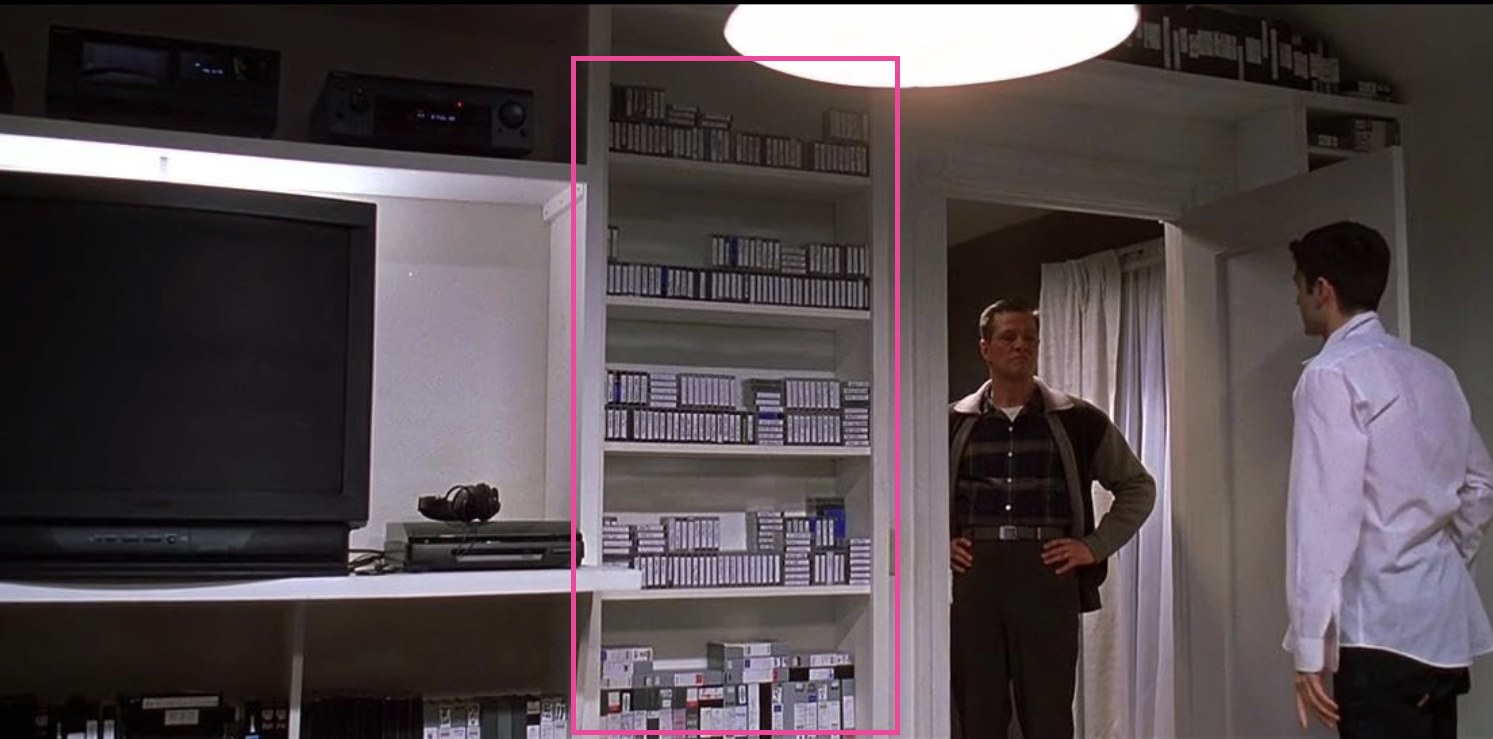 A bedroom scene with a wall of shelves holding hundreds of labeled video tapes, a pink markup box drawn around the shelves